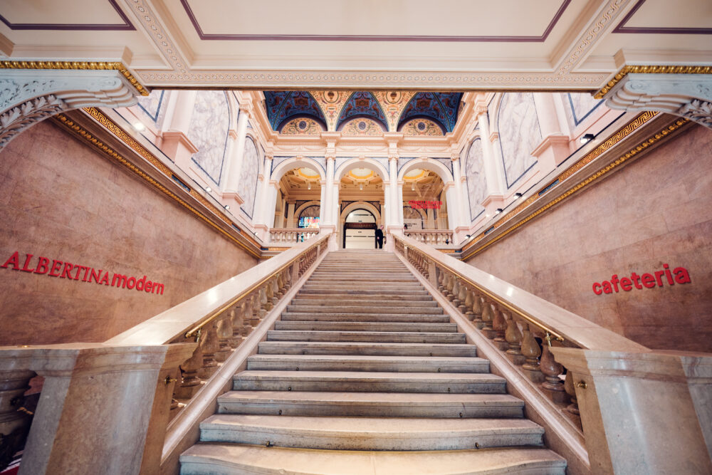 The grand staircase at Albertina Modern museum, with marble steps leading up to elegant arches and a richly decorated ceiling