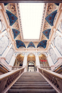 The grand staircase inside Albertina Modern museum, leading up to an ornately decorated ceiling with intricate blue and gold patterns.