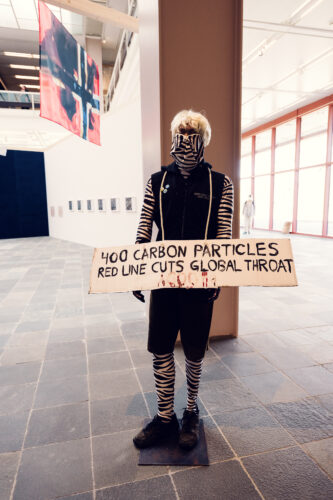 The unique costume and impactful message suggest a performance art piece, highlighting environmental concerns at Belvedere 21.