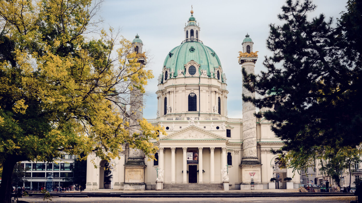 The stunning St. Charles Church (Karlskirche) in Vienna, a baroque church with a large green dome and two ornate columns on either side of its entrance.