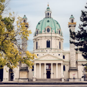 La Chiesa di San Carlo Borromeo (Karlskirche) a Vienna, chiesa barocca con una grande cupola verde e due colonne riccamente scolpite ai lati dell'ingresso.