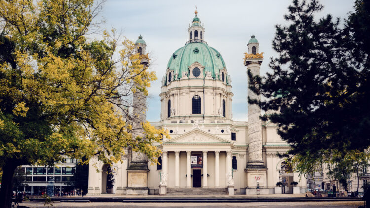 The stunning St. Charles Church (Karlskirche) in Vienna, a baroque church with a large green dome and two ornate columns on either side of its entrance.