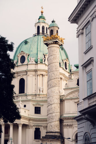 A side view of St. Charles Church (Karlskirche) in Vienna, highlighting one of the intricately carved columns and the green dome.