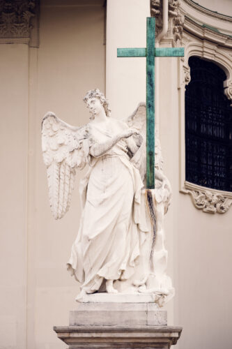 A statue of an angel holding a green cross in front of the St. Charles Church (Karlskirche).