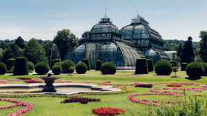 Stunning panoramic view of Schönbrunn's Palm House rising majestically behind a vibrant carpet of seasonal blooms.