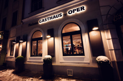 Evening winter scene at Plachutta zur Oper, where falling snow creates enchanting atmosphere around iconic restaurant facade.