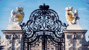 Sun-drenched ceremonial gateway at Belvedere Castle, where guardian sculptures and decorative ironwork shine against deep blue sky.