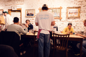 A staff member, wearing a shirt that reads "Von Oma gemacht" ("Made by Grandma"), adding to the café’s homely, nostalgic charm