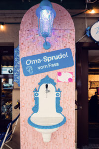 A drinking fountain at Vollpension labeled "Oma-Sprudel vom Fass" ("Grandma’s sparkling water from the tap")