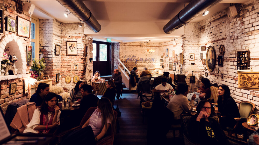 The cozy, rustic interior of Vollpension in Vienna, with exposed brick walls decorated with vintage artwork give the space a warm, nostalgic feel.