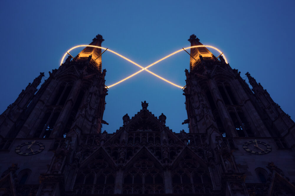 Votive Church in Vienna at dusk, Infinity of Light by Billi Thanner linking the twin towers in a criss-cross glow.
