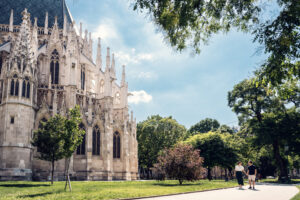 Adriana and Mario strolling near Votivkirche Vienna, with the church's detailed limestone facade and pointed arches creating a dramatic backdrop.