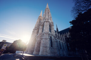 Votivkirche Vienna's neo-Gothic architecture with pointed spires and limestone exterior gleaming in bright summer sunshine on Rooseveltplatz.