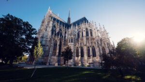 Side view of the Votivkirche (Votive Church) Vienna showing flying buttresses and detailed stonework with lush summer greenery surrounding the base.