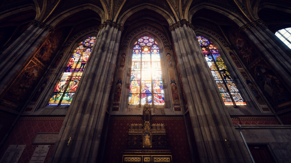 Colorful stained glass windows of Votivkirche Vienna illuminating the stone interior with vibrant light patterns across the neo-Gothic nave.