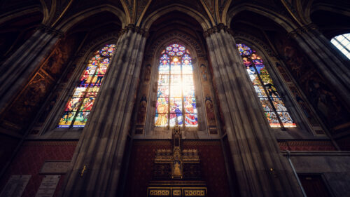 Colorful stained glass windows of Votivkirche Vienna illuminating the stone interior with vibrant light patterns across the neo-Gothic nave.