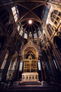 Ornate neo-Gothic main altar of Votivkirche Vienna featuring intricate stone carvings, gold leaf details, and religious sculptures beneath the vaulted choir.