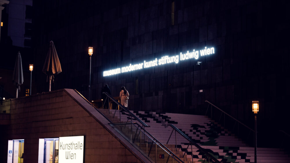 Night perspective of MUMOK Vienna's basalt cube with subtle lighting accentuating the monolithic form in the quieter evening atmosphere of MuseumsQuartier.