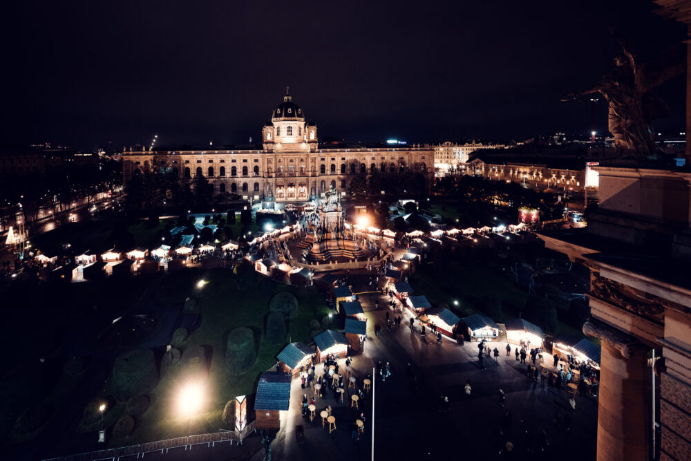 Christmas Market at Maria Theresien Platz Vienna, traditional wooden stalls between the twin museums, decorated with festive lights and holiday ornaments, featuring local crafts and seasonal treats.