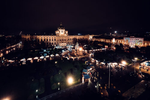 Evening Christmas market at Natural History Museum Vienna (Naturhistorisches Museum Wien), featuring illuminated wooden stalls and museum architecture.