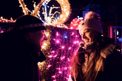 Adriana and Mario standing at a light vendor's stall with handcrafted holiday decorations at the Vienna Rathaus Christmas Market.