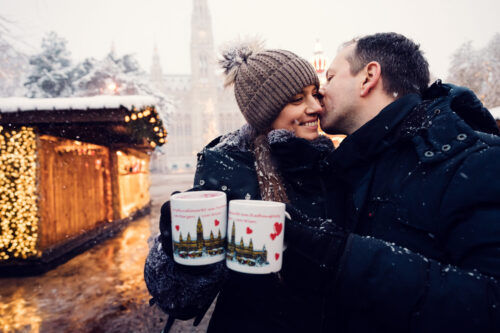Adriana and Mario enjoying traditional punsch at a wooden stall at Vienna City Hall (Rathaus) Christmas Market with the illuminated neo-Gothic facade in the background.