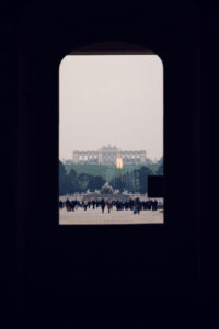 View of Gloriette from Schönbrunn Palace window, baroque imperial palace gardens with formal landscaping leading to historic Gloriette structure.