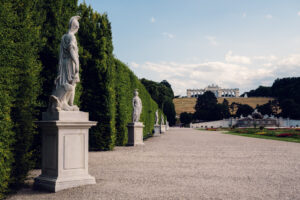 Allegorical garden statue Schönbrunn with weathered stone figure and decorative baroque base surrounded by formal garden pathways.