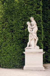 Allegorical garden statue Schönbrunn with weathered stone figure and decorative baroque base surrounded by formal garden pathways.