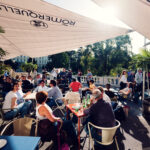 Terrazza affollata del Palmenhaus con ospiti seduti sotto gli ombrelloni.