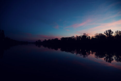 Atmospheric terrace scene at Das Bootshaus during sunset, when the sky reflects golden hues in the water.