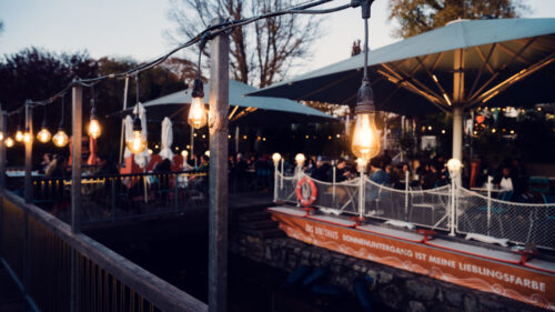 Evening illumination at Das Bootshaus terrace, where string lights create magical moments above the water.