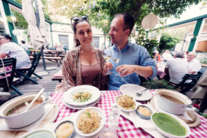 Adriana and Mario with glasses of Gemischter Satz wine, framed by traditional Heuriger decor.
