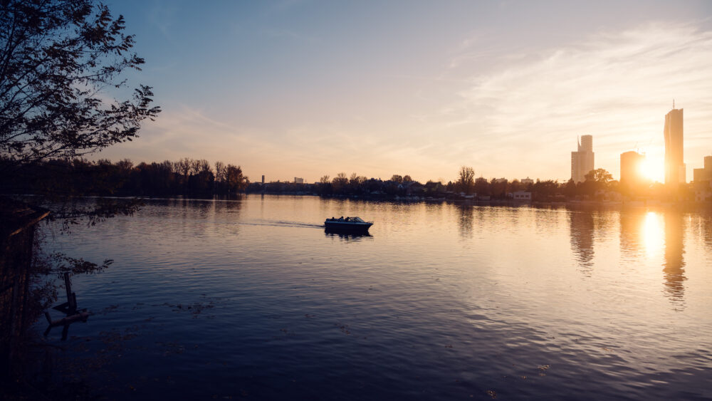 Boot auf der Alten Donau in der Abenddämmerung mit der im Hintergrund leuchtenden Wiener Stadtsilhouette.