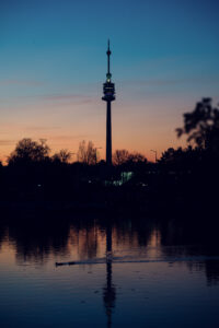 Wiener Stadtsilhouette beim Sonnenuntergang von der Alten Donau mit dem Donauturm als Silhouette gegen den orangen Himmel.