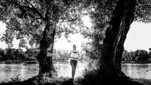 Adriana posing by tree at Alte Donau Vienna with calm river water and natural waterfront landscape in background.