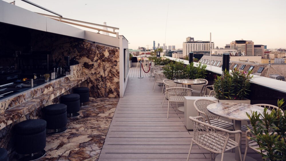 Atmosphere Rooftop Bar's outdoor seating arrangement featuring tables and bar stools facing city view.