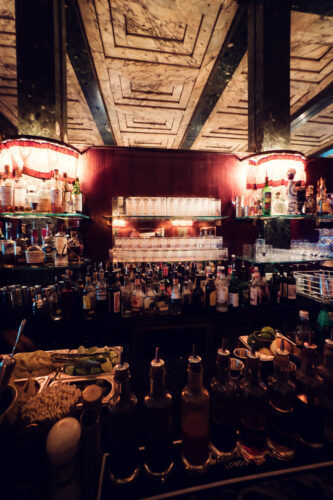 Elegant spirit display at Loos Bar, where historic brass fixtures illuminate premium bottles against modernist design elements.