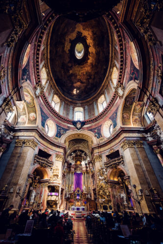 Interior of Peterskirche Vienna (St. Peter's Church) with ornate Baroque dome fresco by Johann Michael Rottmayr, gilded stucco decorations, and dramatic natural light illuminating the central altar.