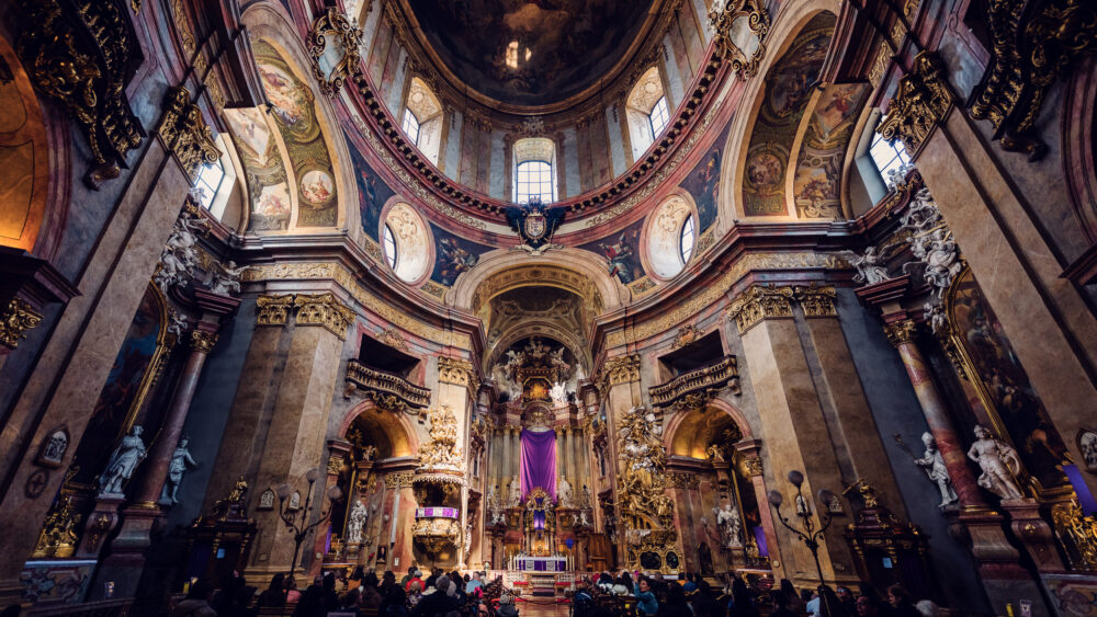 Richly decorated interior of St. Peter's Church Vienna (Peterskirche) featuring elaborate marble columns, intricate pulpit carvings, and the famous oval-shaped floor plan characteristic of Baroque church architecture.