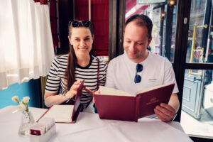 Adriana and Mario examining the traditional menu at Café Sacher Vienna with the historic interior and elegant décor visible in the background.