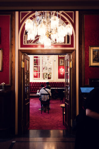 Luxurious interior of Café Sacher Vienna with crystal chandeliers, red velvet upholstery, and polished marble tables where Emperor Franz Joseph once dined, showcasing authentic Viennese coffeehouse elegance.