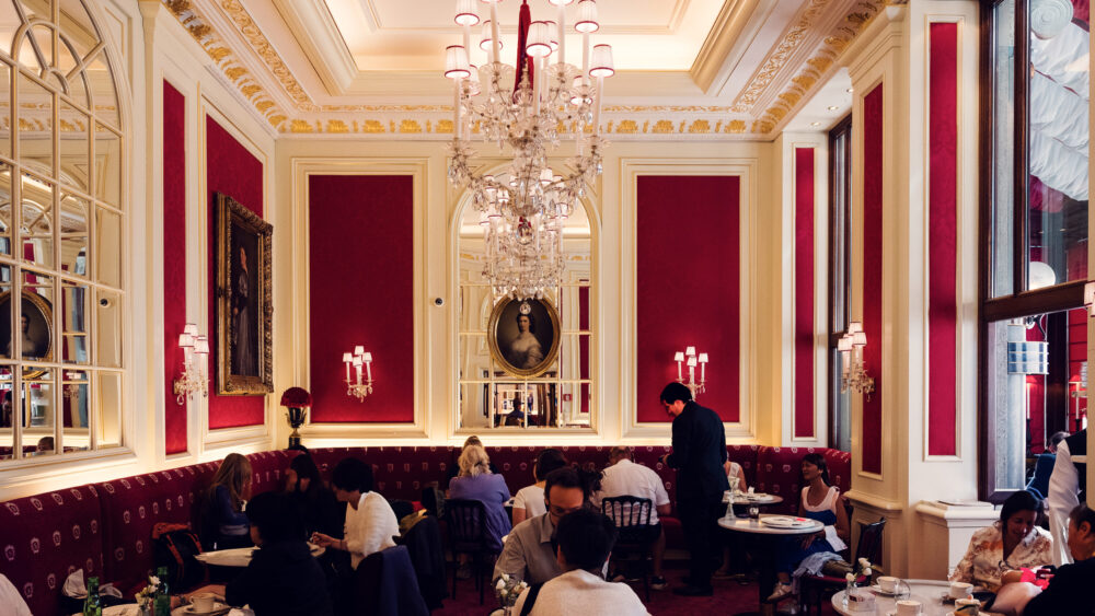 Elegant interior of Café Sacher Vienna with red velvet chairs, crystal chandeliers and classic marble tables.