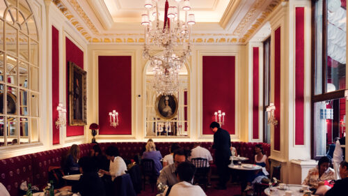Elegant interior of Café Sacher Vienna with red velvet chairs, crystal chandeliers and classic marble tables.