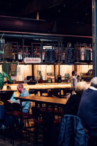 Communal dining experience inside Gleis//Garten Vienna with long wooden tables arranged throughout the spacious interior, surrounded by diverse food stalls offering international cuisine.