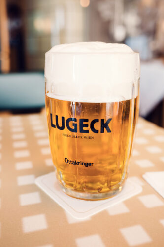 Traditional Austrian beer served at Lugeck Figlmüller restaurant Vienna, golden lager in glass with foam head on wooden table, authentic Viennese dining experience.