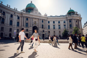 Adriana und Mario schlendern über den Michaelerplatz mit der markanten grünen Kuppel des Michaelertrakts im Hintergrund.