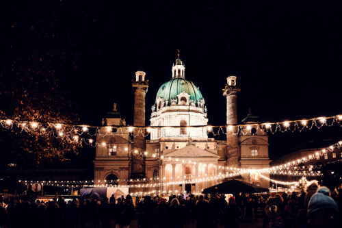 Evening view of illuminated Karlskirche (St. Charles Church) with Art Advent market on Karlsplatz.