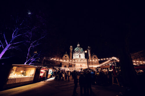 Art Advent market stalls on Karlsplatz with Baroque Karlskirche (St. Charles Church) dome in background.