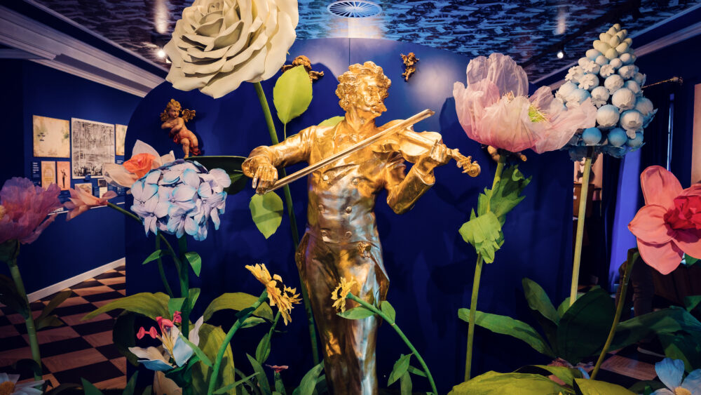 Statua dorata di Johann Strauss che suona il violino circondata da decorazioni floreali oversize.